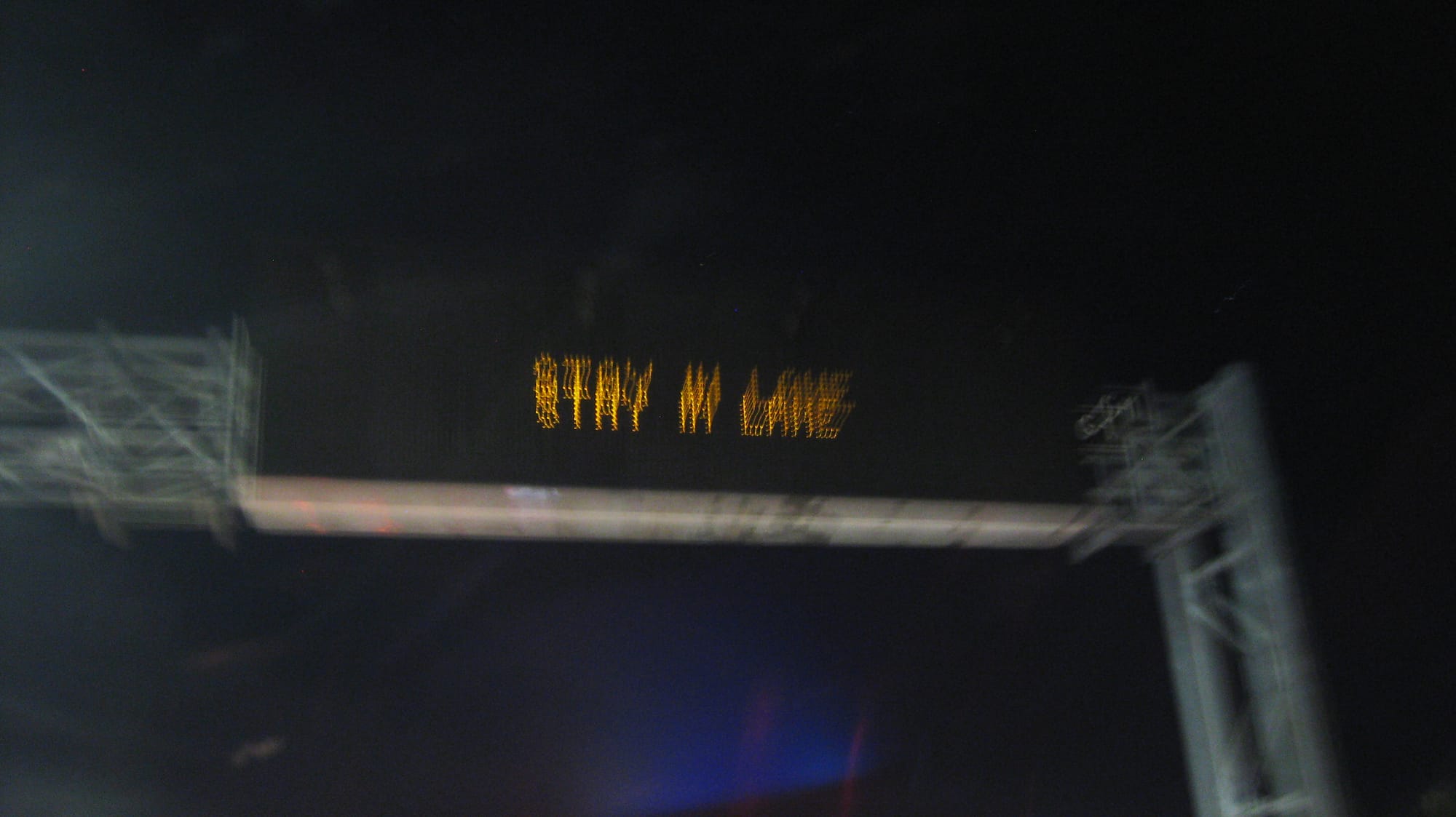 A motion-blurred photograph of a highway sign reading STAY IN LANE, taken at nighttime.